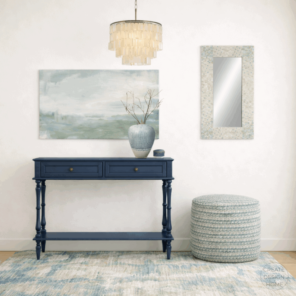 Coastal entryway featuring a soft blue console table, layered artwork, woven ottoman, and subtle coastal textures
