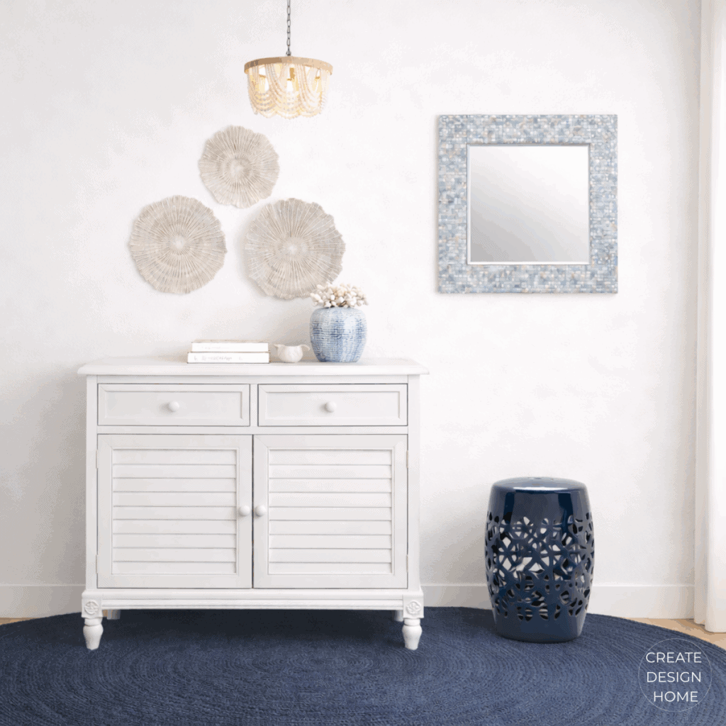 Coastal entryway featuring a white storage cabinet, blue accents, textured wall art, and sculptural coastal accessories