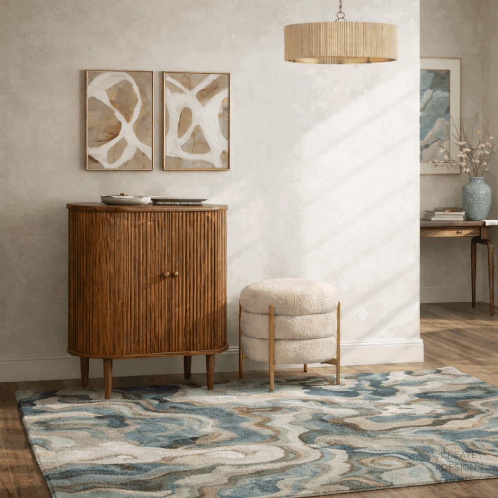 Transitional entryway with a curved wood cabinet, abstract neutral artwork, textured rug, and upholstered ottoman in warm tones.