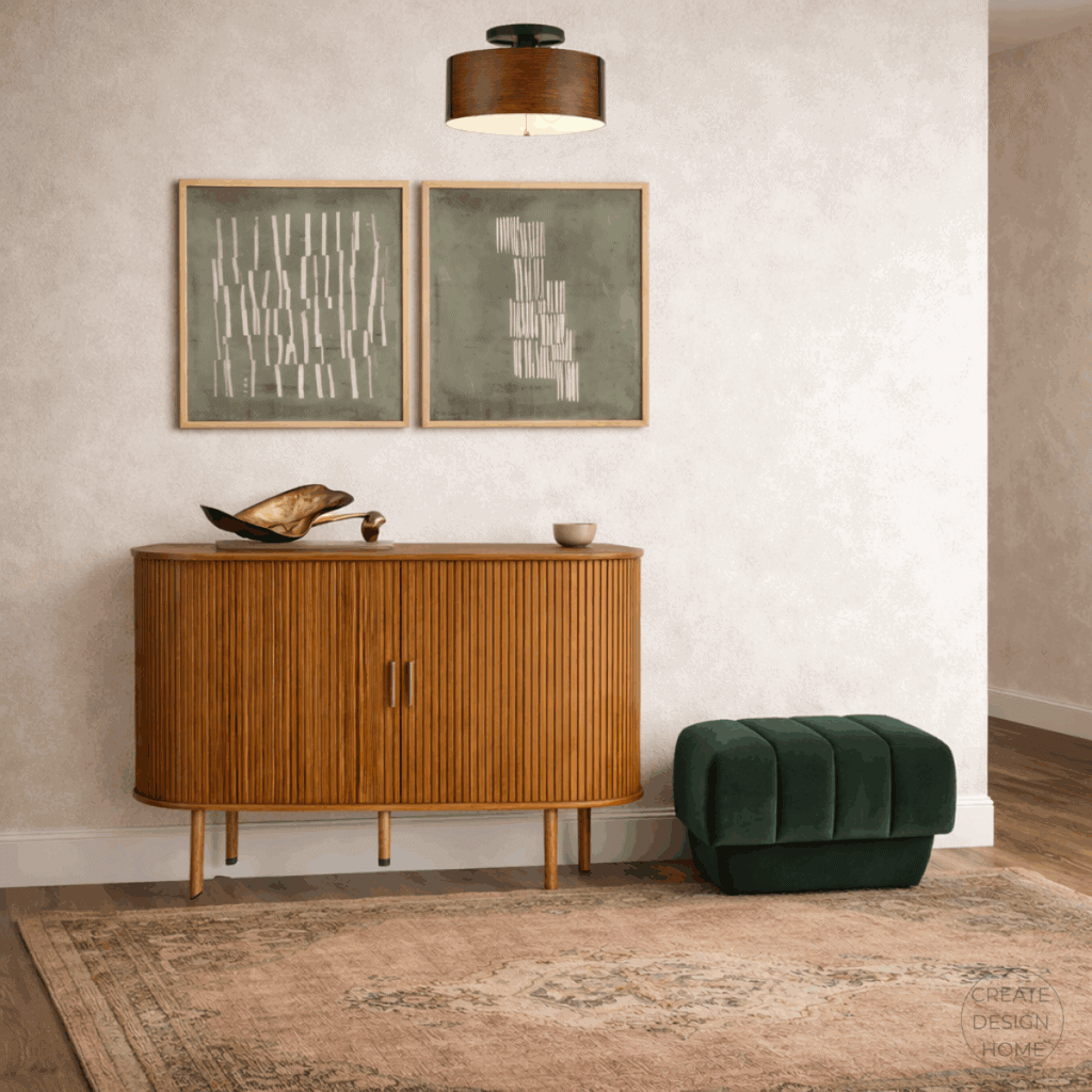 Transitional entryway featuring a warm wood storage cabinet, muted green artwork, a deep green upholstered stool, and a neutral patterned rug.