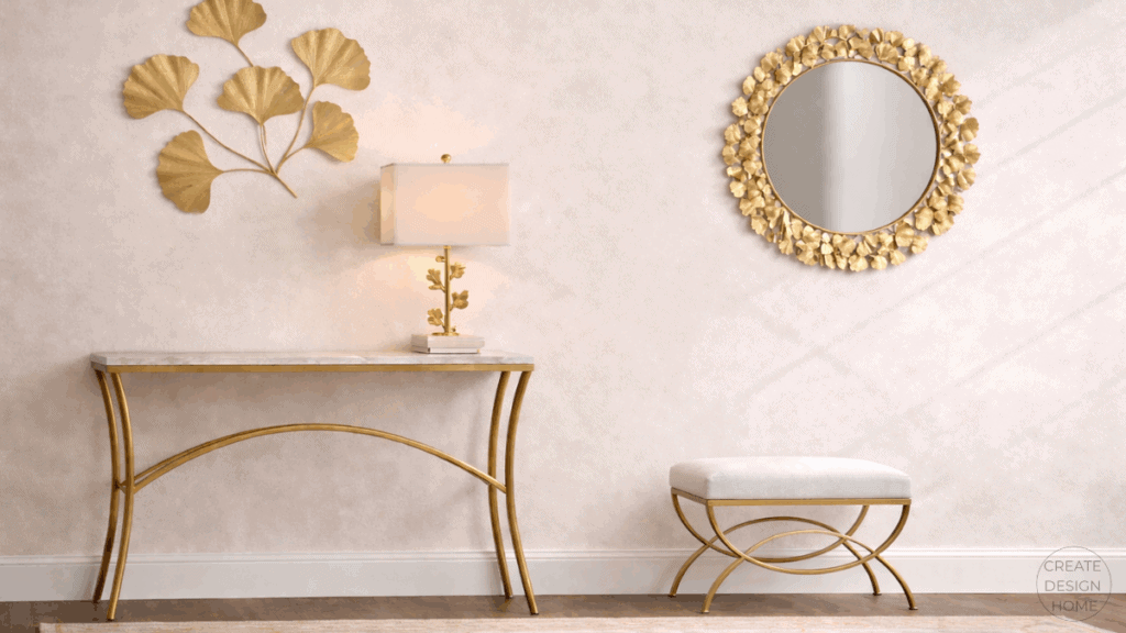 Transitional entryway design featuring a gold-framed console table, upholstered bench, sculptural wall art, and a round mirror in warm neutral tones.
