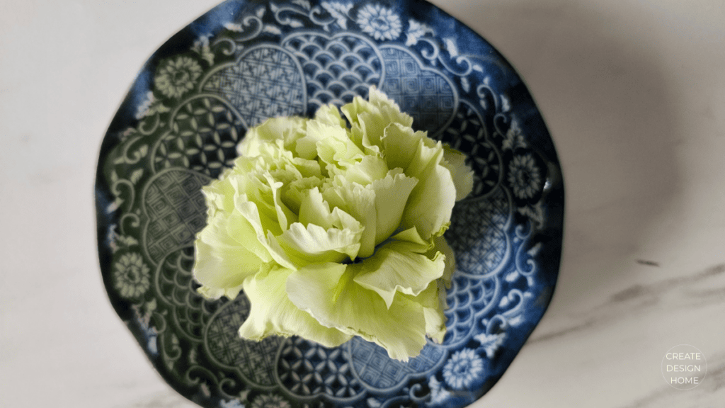 Green flower in a blue patterned bowl representing Kanso, warm simplicity through restrained natural beauty.