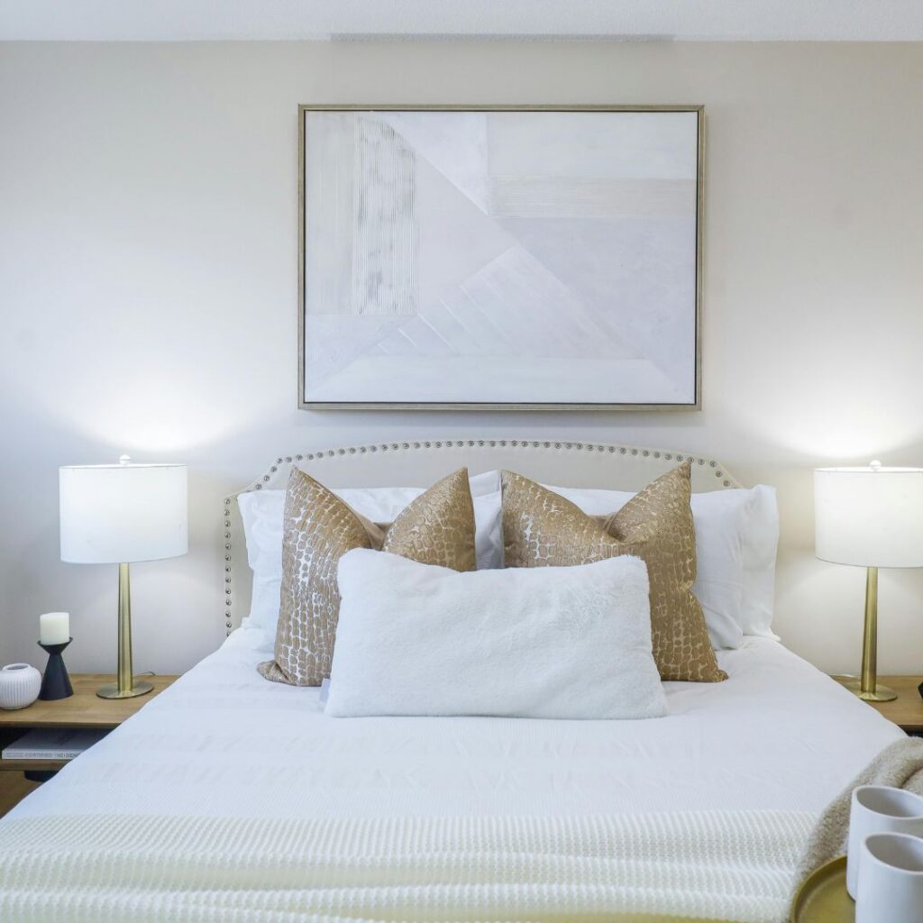 Professionally staged bedroom with layered white bedding, neutral accent pillows, matching bedside lamps and elegant accessories.