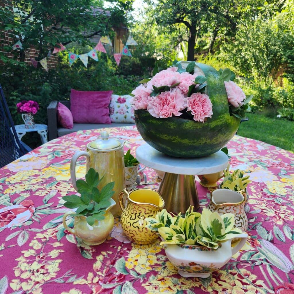 English country garden tea party table with floral tablecloth, colourful tea set and watermelon flower centerpiece