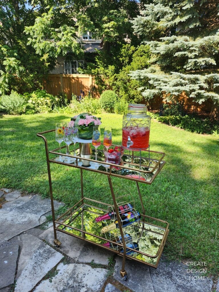 Gold bar cart styled with drinks, flowers and tea party accessories in an English country garden