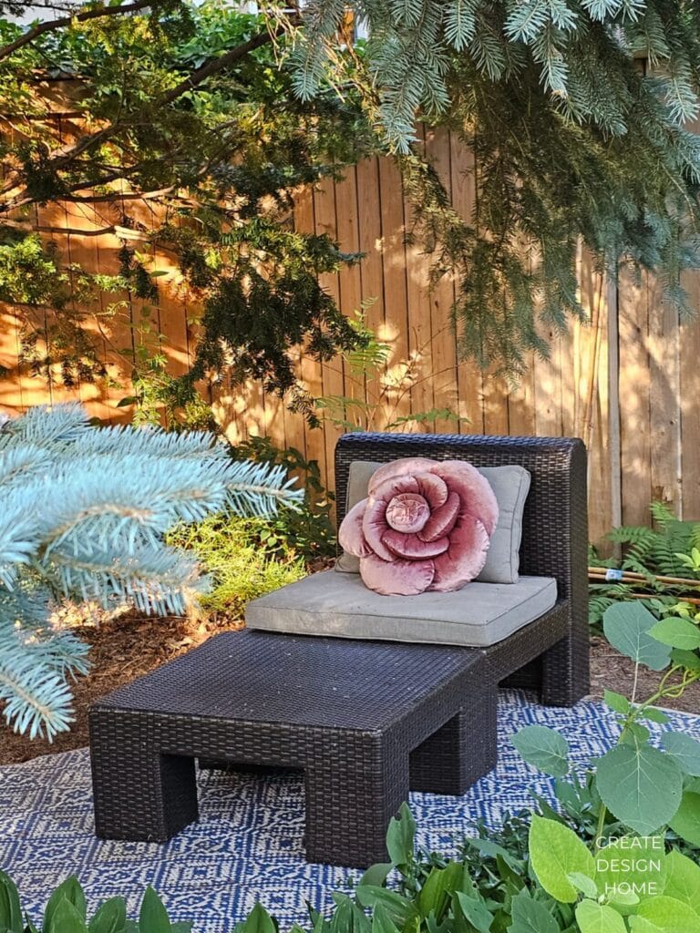 A quiet garden seating area beneath a tree with a floral cushion and outdoor chair