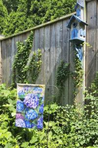 Hydrangea garden flag beside a blue birdhouse in a summer garden