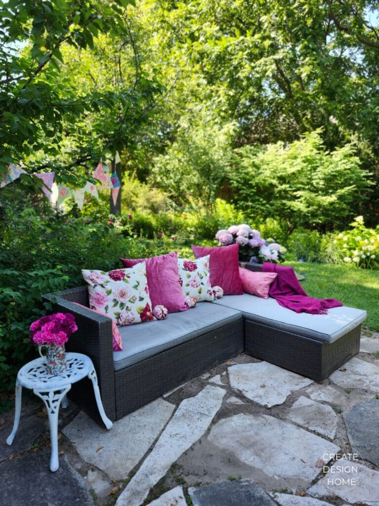 Outdoor lounge area styled with pink velvet cushions, floral pillows and hydrangeas for a summer garden tea party.