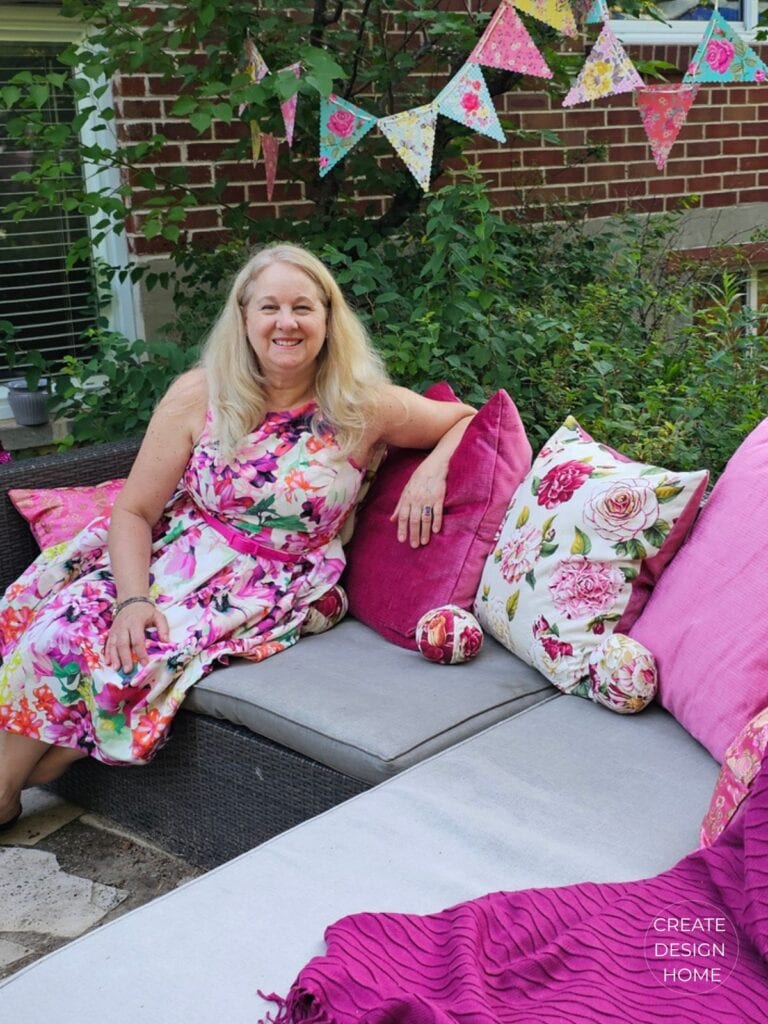 Host relaxing on an outdoor sofa surrounded by pink cushions after hosting a summer garden tea party.