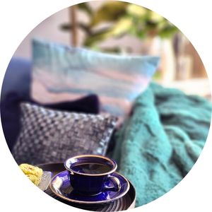 Blue coffee cup on a tray beside cozy cushions, creating a relaxing lifestyle vignette.