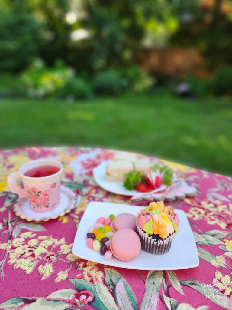Tea sandwiches, floral cupcake, macarons and tea served on a garden table during an English country garden tea party.