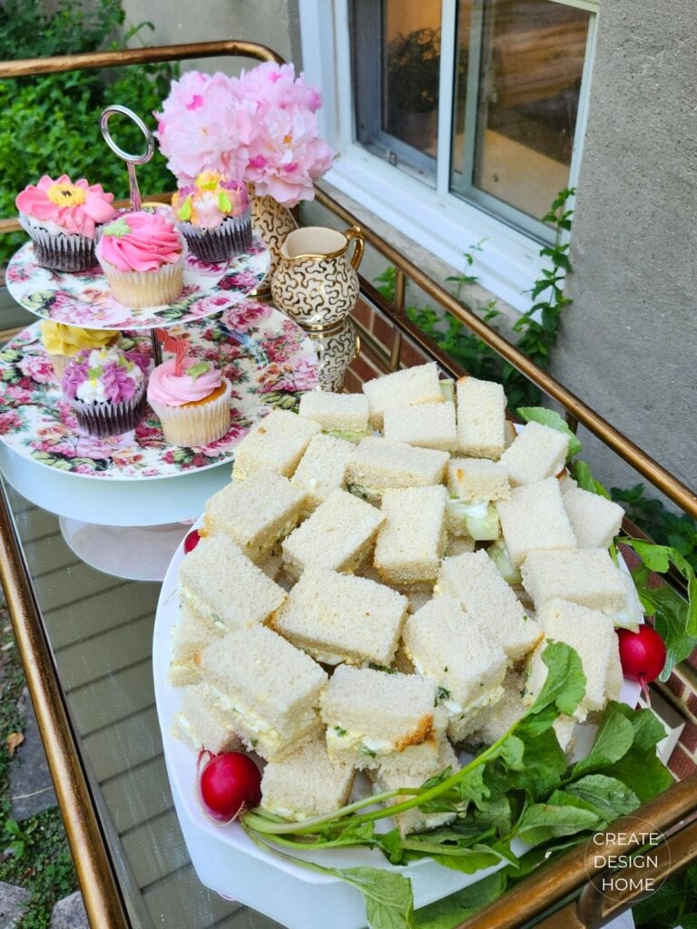 Tea sandwiches and floral cupcakes displayed on a vintage-style beverage cart at an English country garden tea party.