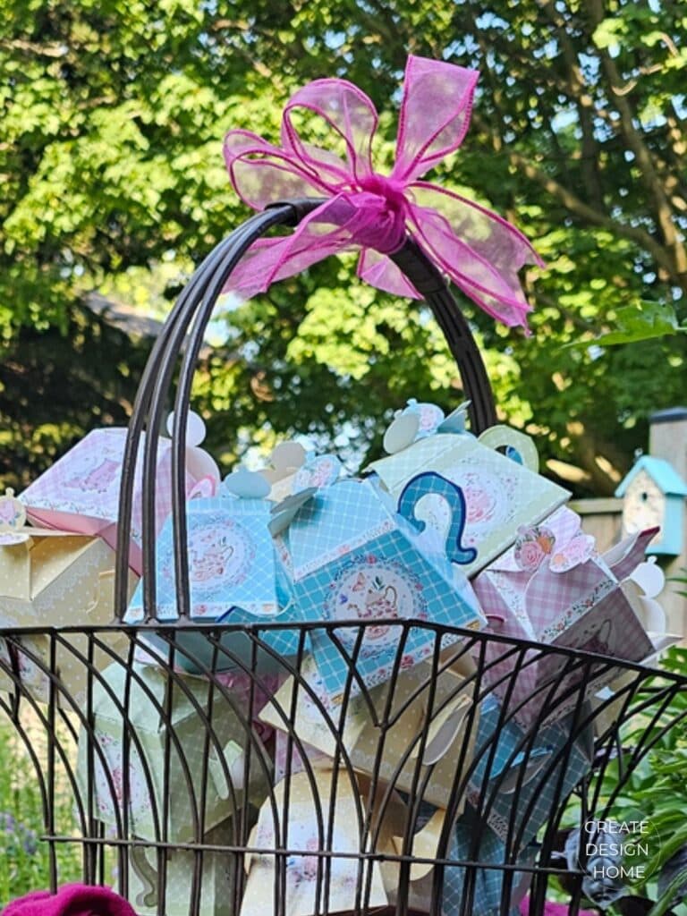 Teapot-shaped party favor boxes filled with jelly beans displayed in a garden basket.