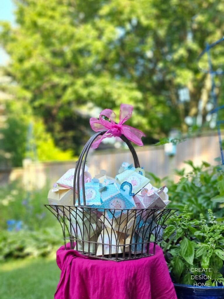 Vintage inspired paper teapot party favor boxes displayed in a garden basket for a summer tea party