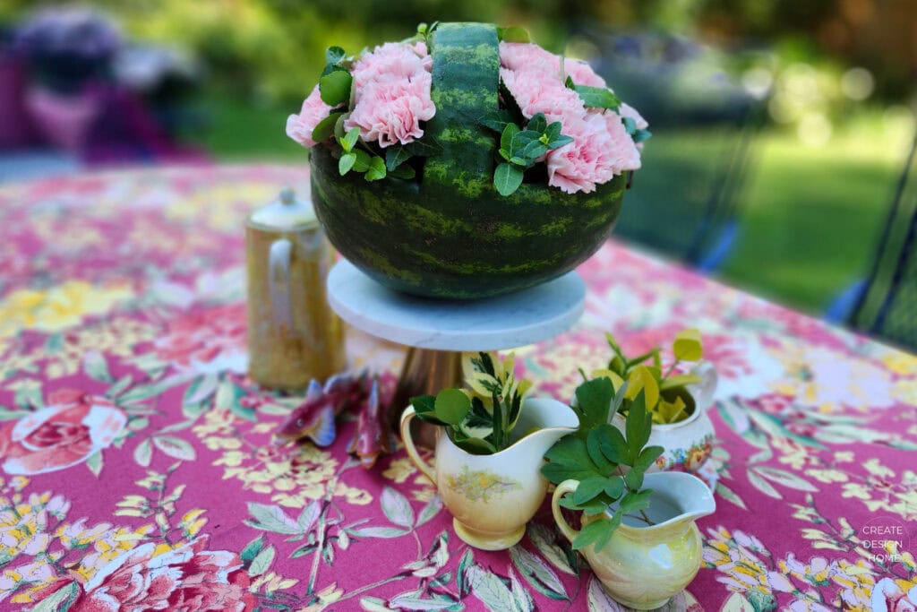 Watermelon floral centerpiece with pink carnations and greenery displayed on a summer garden tea party table