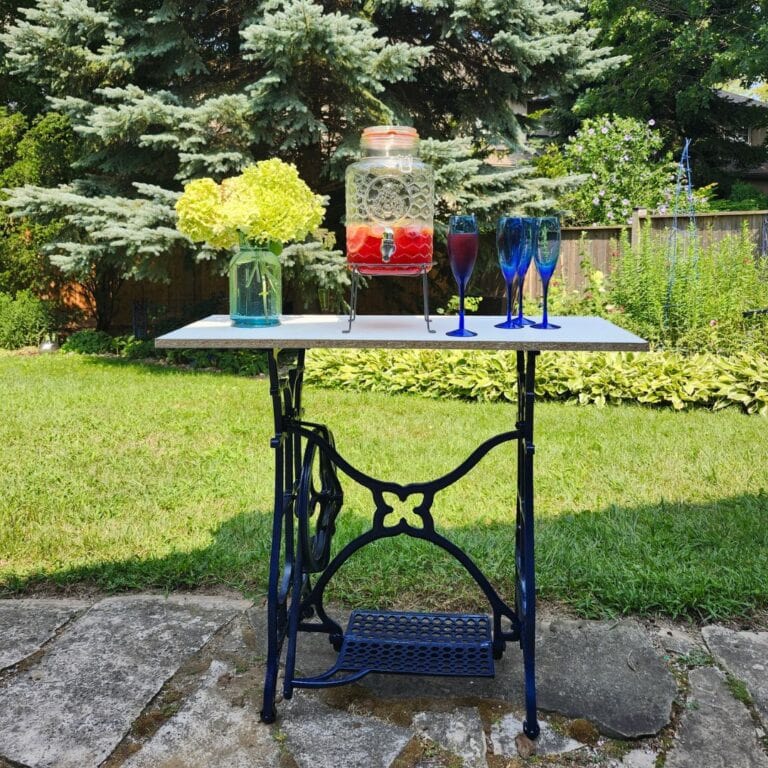 Antique sewing machine base repurposed as an outdoor drinks station with lemon water and blue glasses