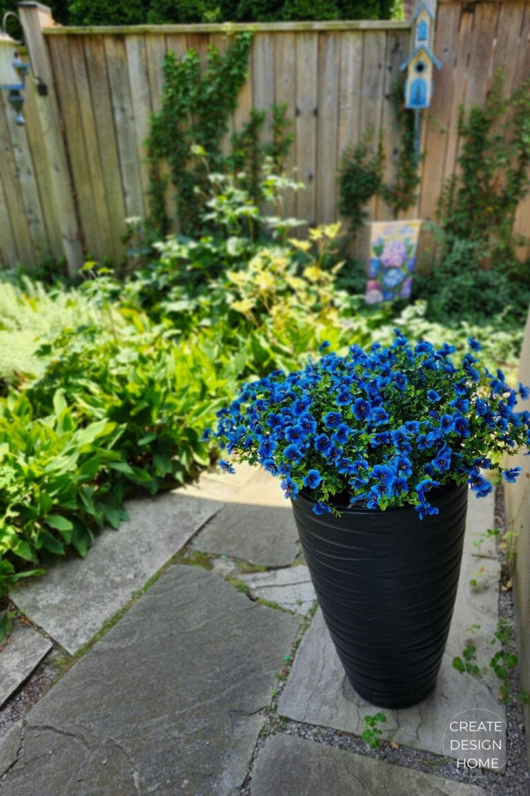 Blue faux flowers in a tall black planter beside a garden patio