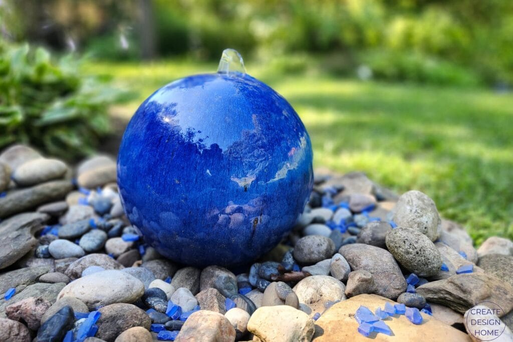 Blue glass sphere water feature surrounded by river rocks and blue glass stones