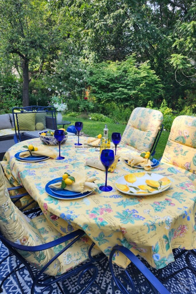 Outdoor lemon-inspired table with yellow floral tablecloth, blue glassware and fresh lemons