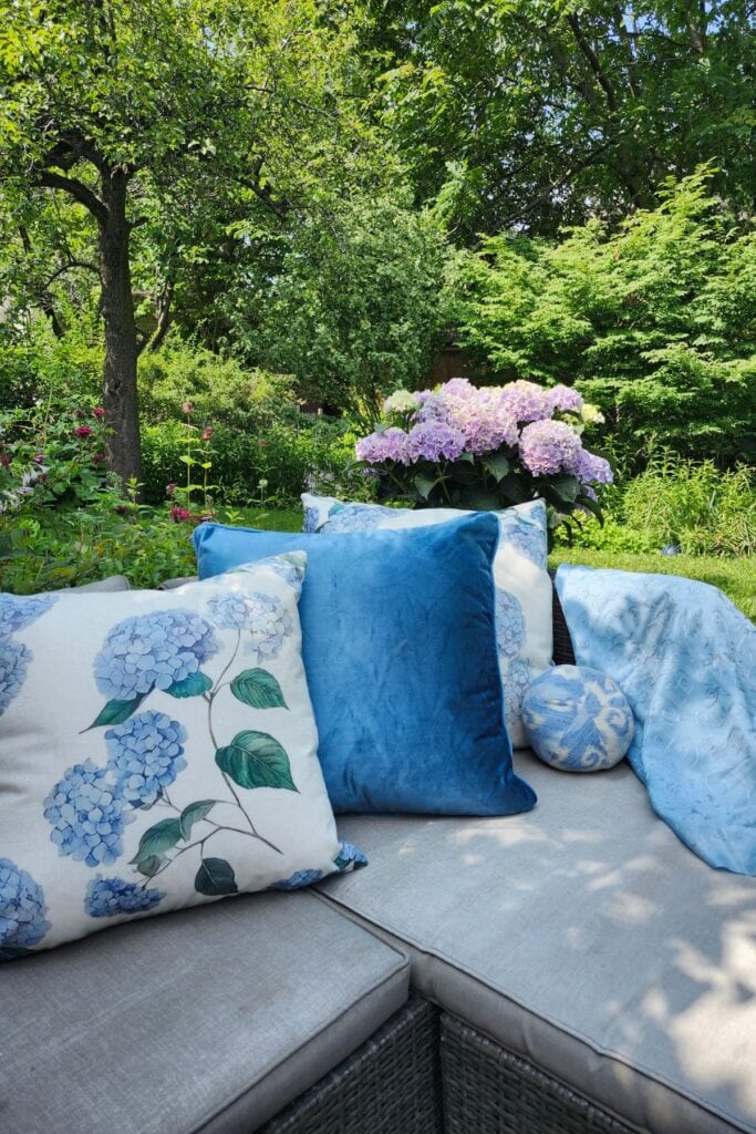 Blue hydrangea cushions and pillows on neutral wicker garden seating.