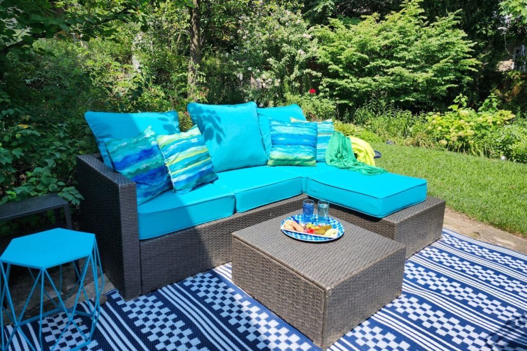Blue outdoor cushions and patterned outdoor rug adding colour to a garden seating area.