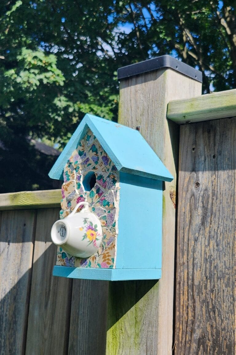 Blue garden birdhouse decorated with a floral teacup and mosaic pieces.