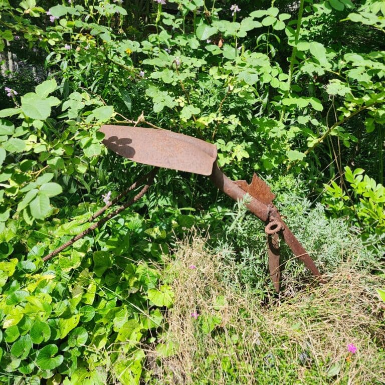Rustic bird garden sculpture made from repurposed shovel and metal tools among green plants.