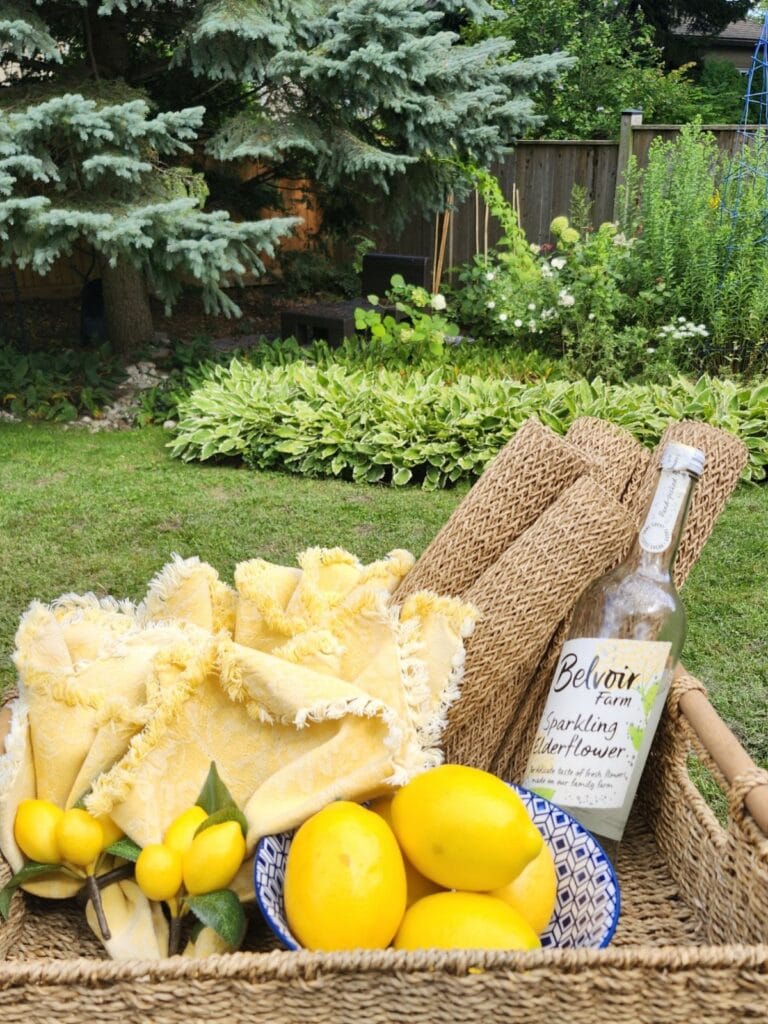 Wicker tray with lemons, yellow throw and decorative bottle styled for a garden party.