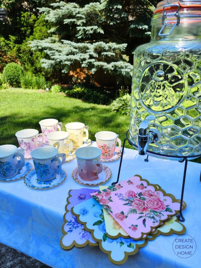 Vintage floral teacups and colourful napkins beside a glass drink dispenser at a summer garden tea party